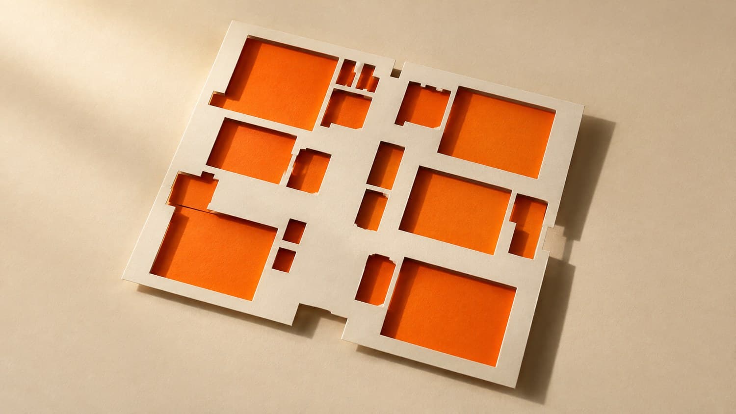 A bone-white exhibition floorplan with its stand spaces punched clean out of the paper, bright orange showing through every opening