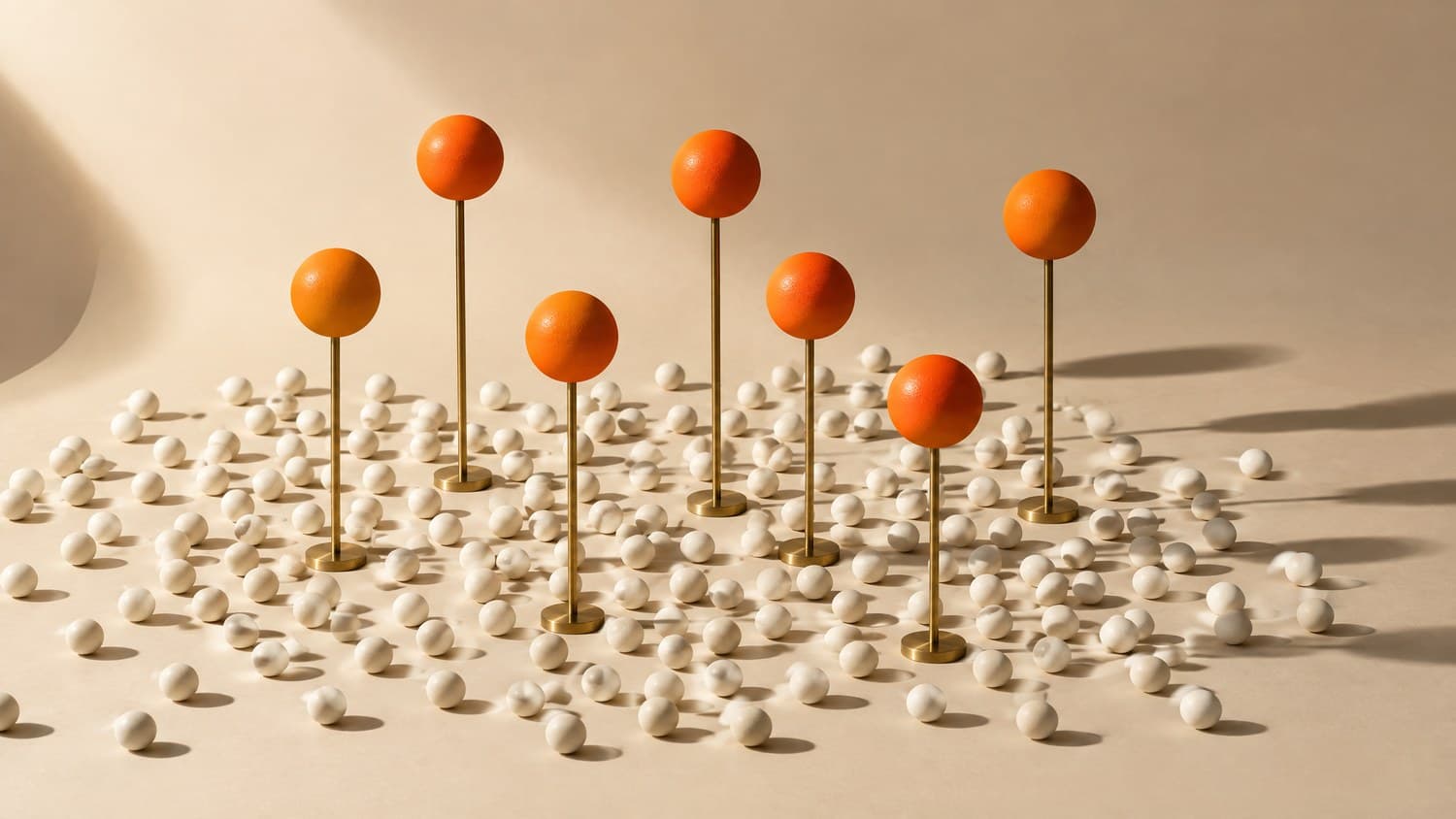 Seven orange spheres raised on slender brass stands above a wide scatter of small bone-white spheres on a bone paper sweep.
